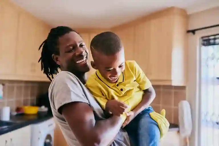 Father holding son enjoying a playful moment while in the kitchen cleaning up.
